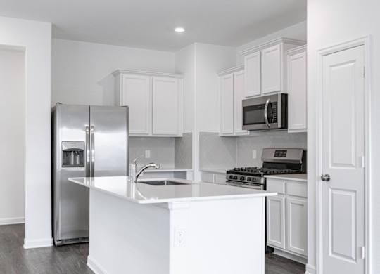 Apartments Humble, TX - Edgewater at the Lagoon - Kitchen with Vinyl Plank Flooring, White Quartz Countertops, White Cabinetry, Stainless Steel Appliances, Grey Herringbone Tile Backplash, and Cooking Island with a Sink.