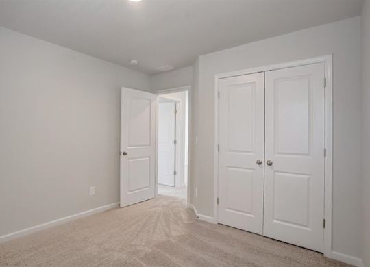 A room with white walls and carpeted floor with two white doors.
