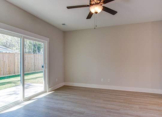an empty living room with a sliding glass door and a ceiling fan