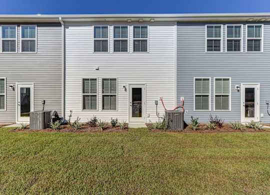 North Charleston, SC Townhomes Near The Citadel - Highland Townhomes - Exterior View of Townhomes with White and Grey Walls, and Backyards with Manicured Grass Lawns.