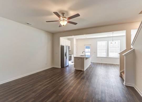 an empty living room with a ceiling fan and a kitchen