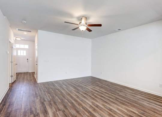 Four-BR Townhomes in North Charleston, SC - Highland Townhomes - Empty Living Room With White Walls, Wood-Style Flooring, and A Ceiling Fan