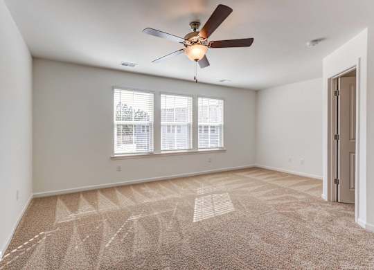 an empty living room with a ceiling fan and three windows