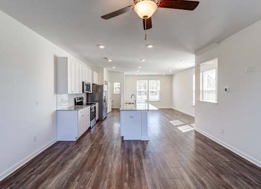 an empty living room with a ceiling fan and a kitchen