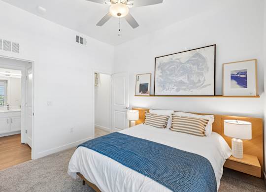 A bedroom with a bed, a ceiling fan, and a painting on the wall.