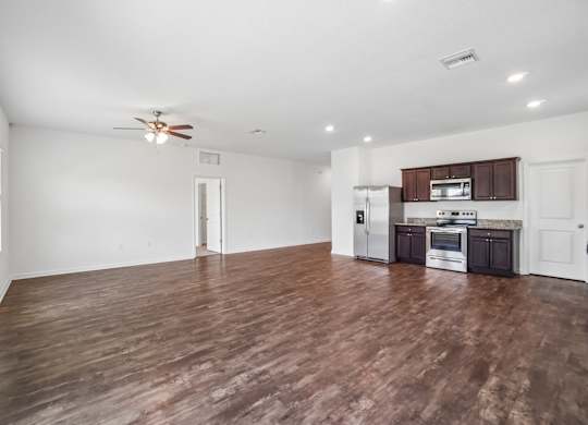 A spacious room with a kitchen area and wooden flooring.