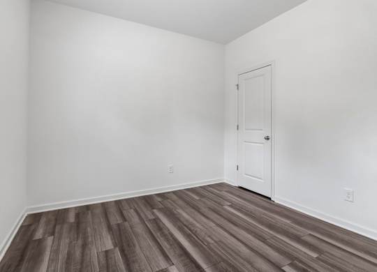 A room with a white door and wooden flooring.