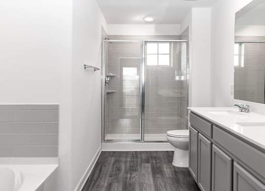 Dog-Friendly Homes for Rent in Humble, TX - Edgewater at the Lagoon - Bathroom with Hardwood Floor, Double Vanity Sink, Gray Cabinetry, Sliding Glass Door Shower, and Separate Bathtub.