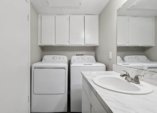 A white laundry room with a sink and cabinets.
