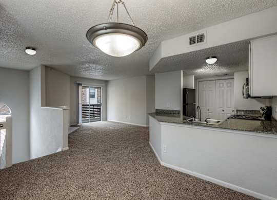 A spacious kitchen and living room with white cabinets and a carpeted floor.