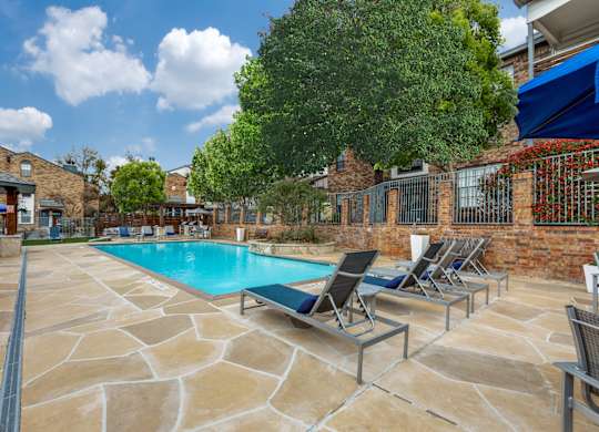 A pool surrounded by chairs and trees.