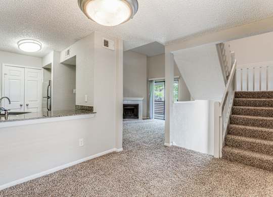 a living room with a staircase and a kitchen in the background