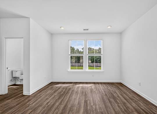 A room with a window showing a view of a fence and trees.