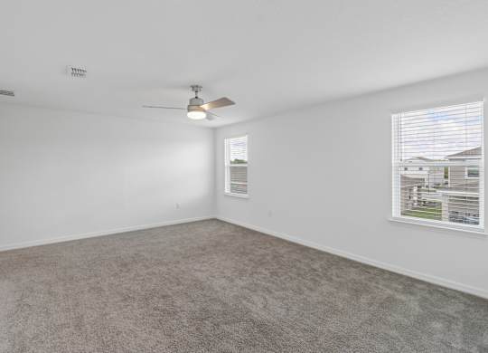 A room with a carpeted floor, a ceiling fan, and a window showing a view of buildings outside.