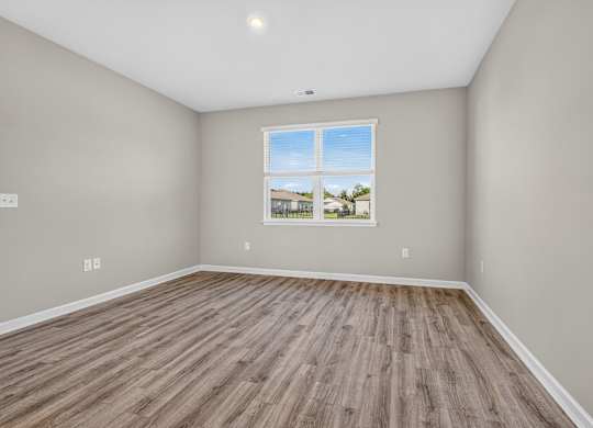 A room with a window showing a view of a house and trees.