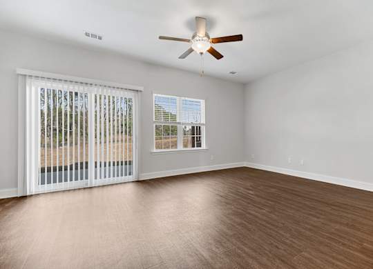Cottonvale Towns in Savannah, GA photo of living room with large windows, ceiling fan, and hardwood flooring