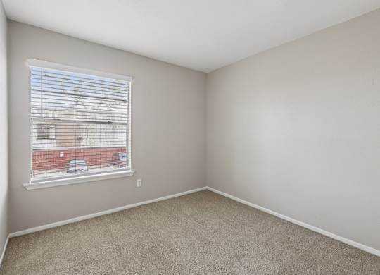 A room with a window and a view of a red building outside.