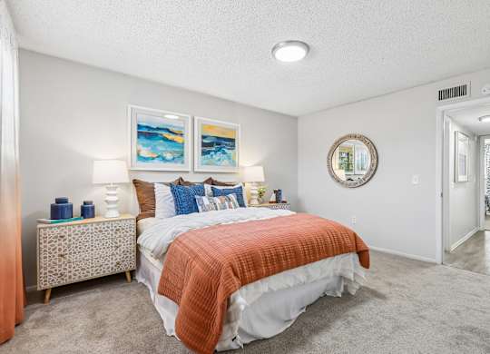 A bedroom with a bed, nightstand, and two paintings on the wall.