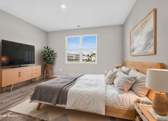 A bedroom with a large bed, a television, and a window with a view of the outdoors.