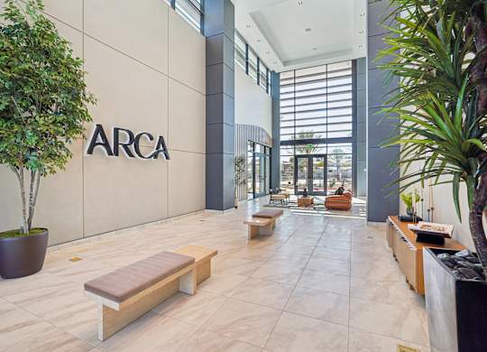 A lobby with a bench and a tree in front of a wall with the letters ARCA on it.