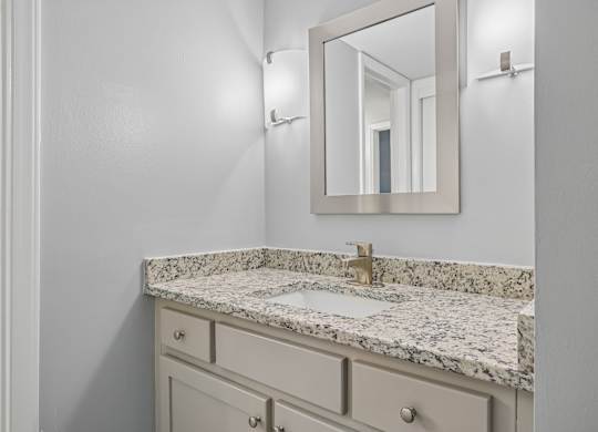 A bathroom with a marble countertop and a mirror above it.