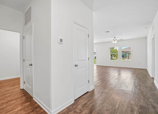 A room with white walls and wooden floors with a door on the left.