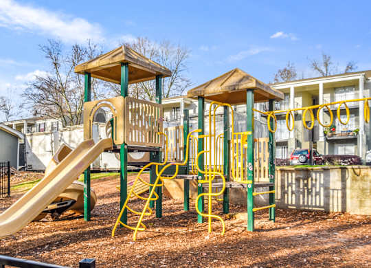 A playground with a yellow slide and a wooden structure.