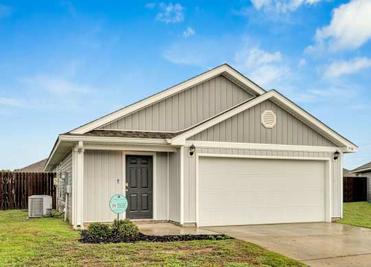 A house with a grey garage door and a sign on the lawn.