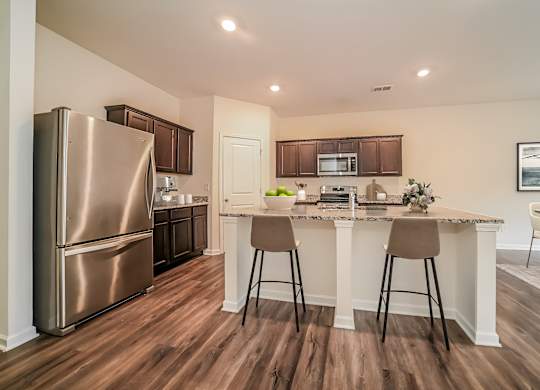 A kitchen with a refrigerator, bar stools, and a countertop.