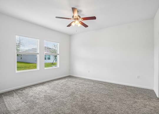 A room with a ceiling fan and two windows.