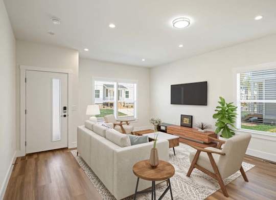A modern living room with a white sofa, a wooden coffee table, and a flat-screen TV mounted on the wall.