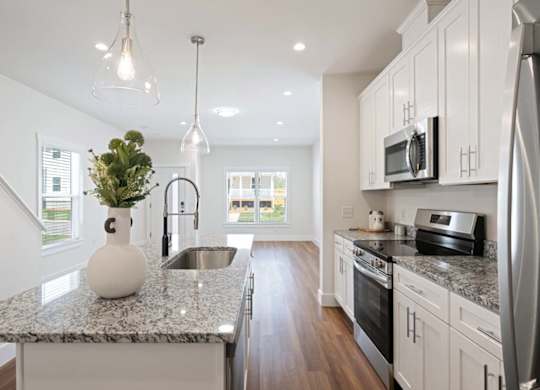 Bright kitchen with granite countertops, stainless steel appliances, pendant lighting, and wood flooring.