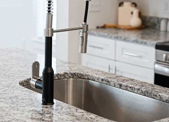 Close-up of a modern kitchen faucet with a pull-down sprayer and granite countertop.
