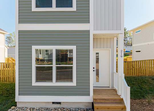 Front entry of a modern two-story home with green siding, large windows, and a small porch.