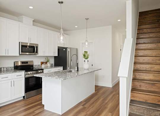 Modern kitchen with white cabinets, center island, stainless steel appliances, and pendant lighting.