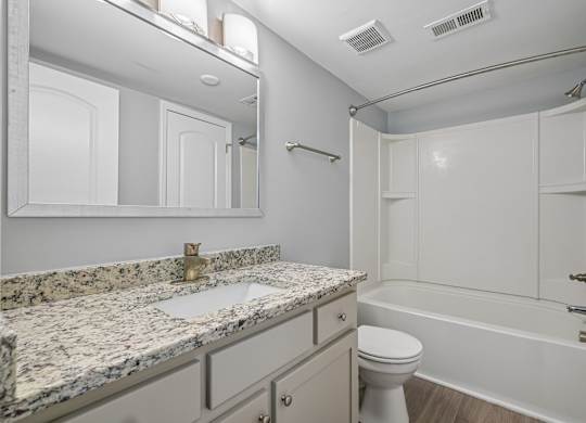 A bathroom with a marble countertop and white fixtures.