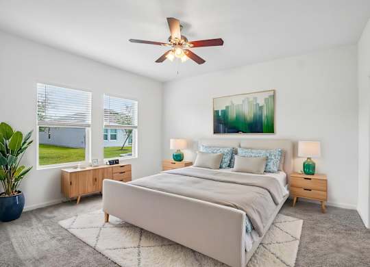 A bedroom with a large bed, a ceiling fan, and a painting on the wall.