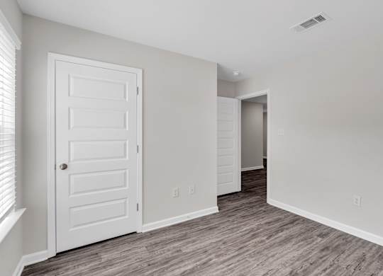 A white door is on the left of a room with a wooden floor.