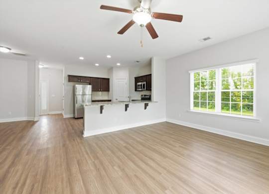 A spacious kitchen and living room with wood flooring and a ceiling fan.