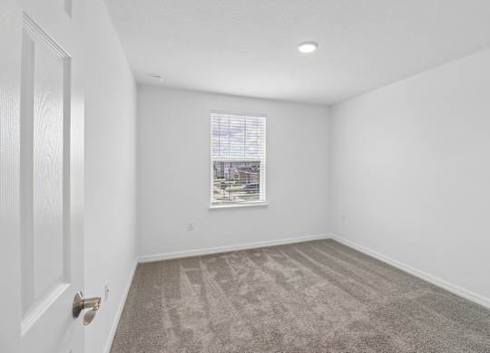 A room with a carpeted floor and a window with blinds.