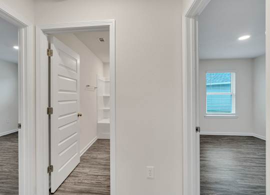 A white door is open to a hallway with wood floors.