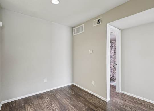 A room with wooden flooring and a doorway leading to another room.