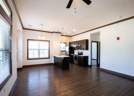 an empty living room with a kitchen and a ceiling fan