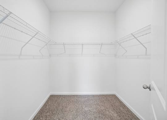 A room with a carpeted floor and a white wall with a door and a coat rack.