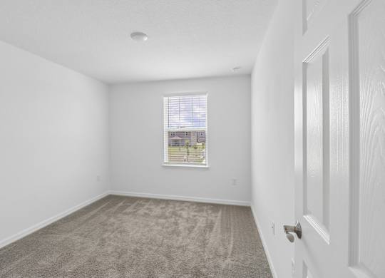 A room with a carpeted floor and a window with blinds.