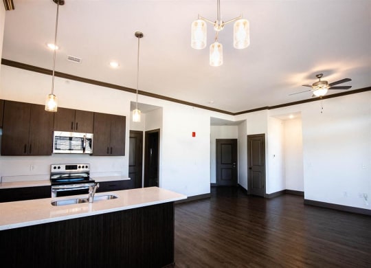 an empty living room with a kitchen and a ceiling fan