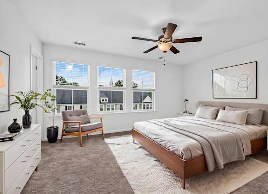 A bedroom with a large bed, a ceiling fan, and a chair.