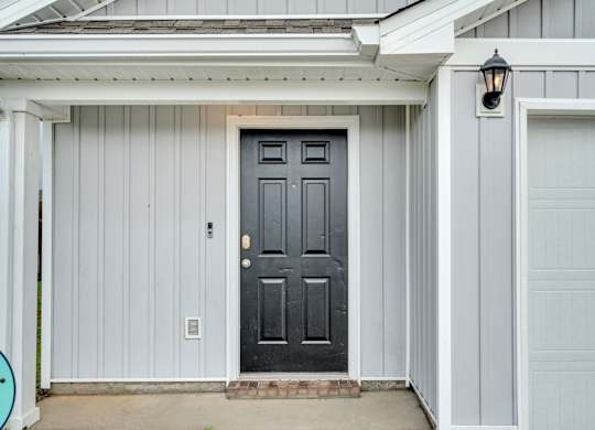 A black door is on the left side of a white garage.