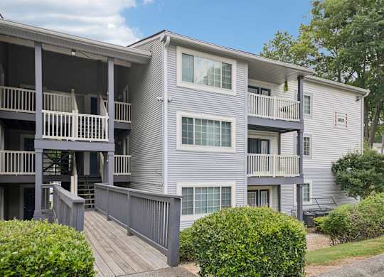 A grey apartment building with a balcony and a small garden.