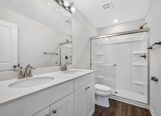 A white bathroom with a double sink and a walk-in shower.